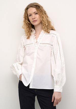 Weiße Baumwollbluse mit einem Rüschensaumkragen, dekorativen Spitzenakzenten an Schultern und Ärmeln sowie Knopfverschlüssen auf der Vorderseite.
