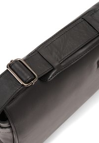 Schwarze Leder-Umhängetasche mit glatter Textur, ausgestattet mit einer Metall-Schnalle am Gurt und einem minimalistischen Design.