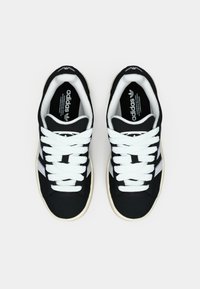 Par svart-hvite Adidas joggesko med hvite lisser og logo, sett ovenfra på hvit bakgrunn.