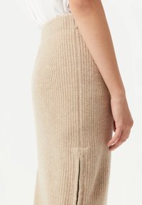 Beige ribbad stickad kjol med en figurnära design och sidoklipp, som visar en mjuk textur och en längd till mitt vad.