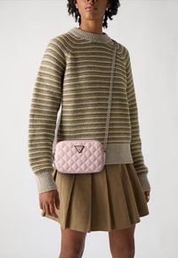Light pink quilted shoulder bag with a chain strap and logo detail, paired with a striped sweater and pleated olive green skirt.