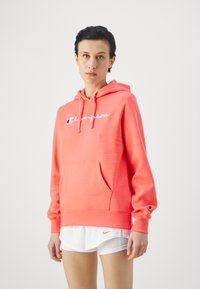 Felpa corallo in misto cotone, con tasca centrale a marsupio e logo "Champion" bianco sul petto. Polsini e orlo a costine.