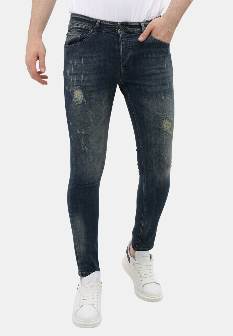 Skinny-fit denim jeans in diepblauw, met versleten details en scheuren. Gecombineerd met witte sneakers.