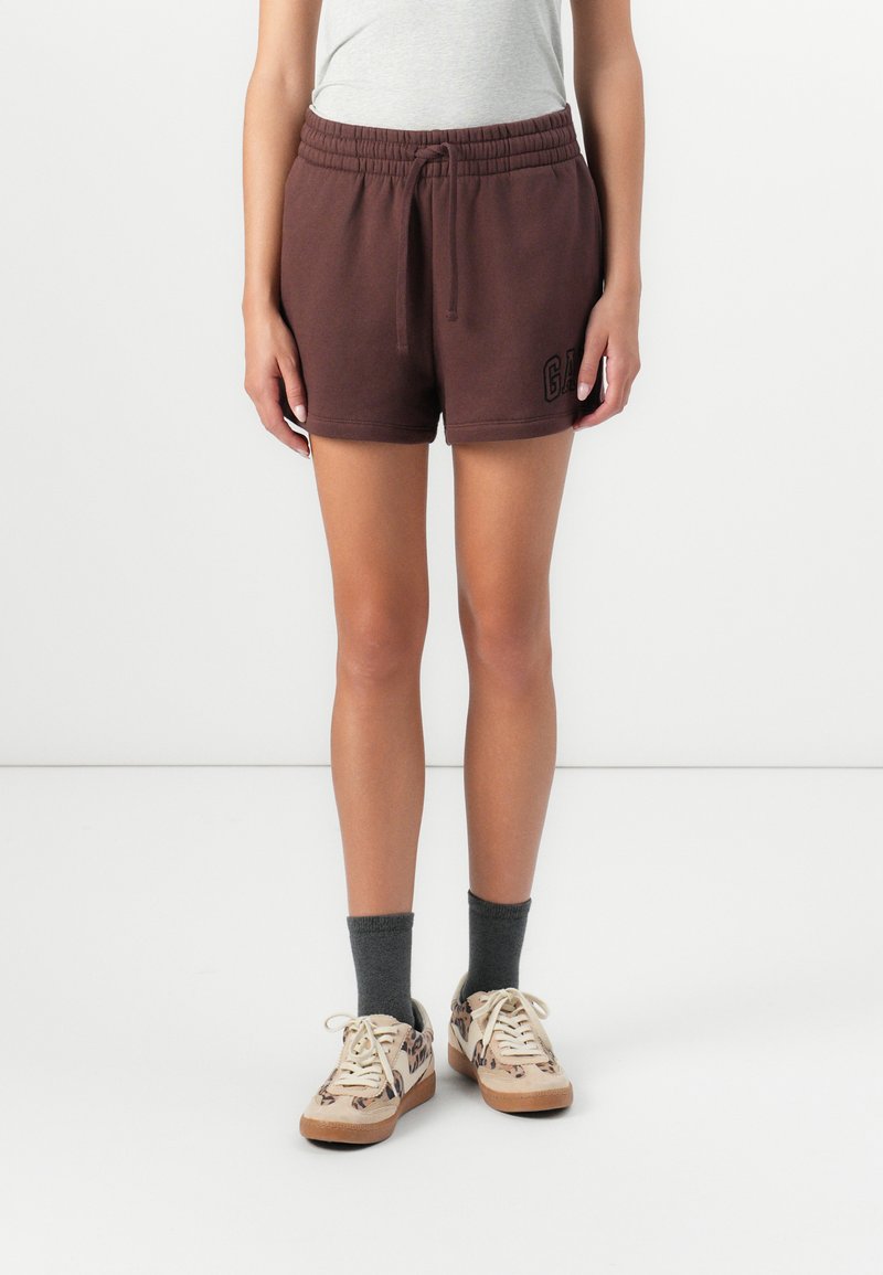 Brune shorts med elastik i taljen og sidelommer har "GAP" logo i sort. Sættes sammen med grå sokker og mønstrede beige sneakers.