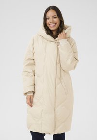 Beige puffjakke med hætte, med et diamantmønstret quiltet design, oversized pasform og lommer. Glat, blødt stof med ribbede manchetter.