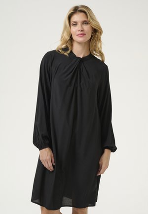 Robe noire à manches longues avec un col froncé et des poignets élastiques. Tissu lisse avec une forme évasée, tombant juste au-dessus des genoux.