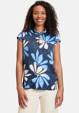 Blusa floreale blu navy con scollatura rotonda, maniche corte e dettaglio a chiave. Il tessuto ha una consistenza liscia e bold con motivi bianchi e blu.
