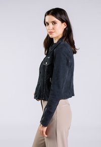 Giacca di jeans nera accorciata, con hardware argentato, chiusure a bottoni, due tasche frontali e tessuto testurizzato con una leggera lucentezza.