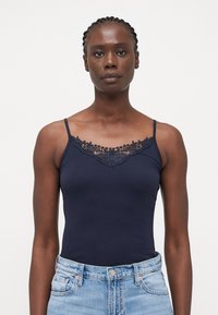 Navy camisole dengan hiasan renda di leher, terbuat dari katun elastis. Memiliki tali tipis dan desain ketat.