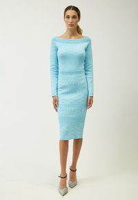 Helles blaues Strickkleid mit schulterfreier Gestaltung, langen Ärmeln und figurbetontem Schnitt. Das Wort "INFLUENCER" ist durchgehend im Muster dargestellt.