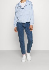 Vaaleansininen huppari, jossa on etutasku, elastiset hihansuut ja kiristettävä helma, yhdistettynä tummansinisisiin farkkuihin ja valkoisiin tennareihin.