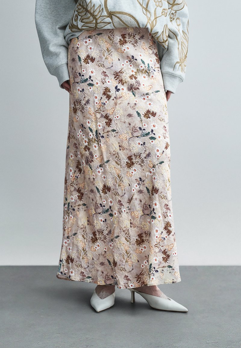 Μίντι φούστα με λουλουδάτο σχέδιο σε απαλό μπεζ, με περίπλοκη κεντητική σε αποχρώσεις καφέ, πράσινου και λευκού. Ομαλή υφή, σε συνδυασμό με λευκές γόβες.