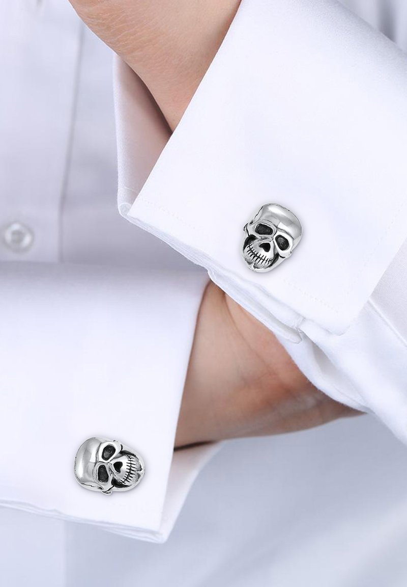 Silver skull cufflinks attached to a white dress shirt. The design features intricate facial details and a polished metallic finish.