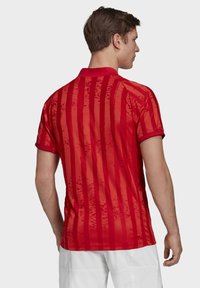 Camisa polo roja con rayas verticales de diferentes texturas, un cuello sólido y mangas cortas. El material parece suave y ligero.
