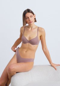 Mauve beha en bijpassend bikinisetje van gladde stof; voorzien van dunne bandjes, minimalistisch ontwerp en naadloze afwerking.