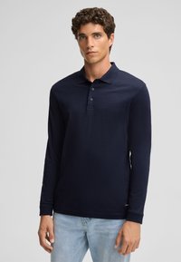 Granatowa, długosleeve polo z klasycznym kołnierzykiem, trzema guzikami oraz fakturowanym materiałem; w zestawieniu z jasnoniebieskimi dżinsami.