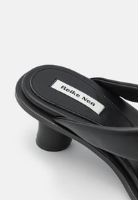 Sandale noire à talon avec talon bloc arrondi et semelle intérieure rembourrée affichant une étiquette blanche avec le texte "Reike Nen".