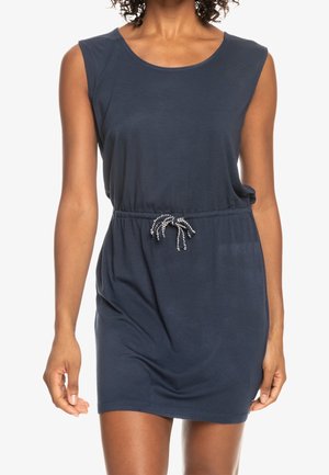 Femme portant une robe décontractée sans manches bleu marine avec une taille à cordon, présentée du cou jusqu'à mi-cuisse sur un fond blanc.