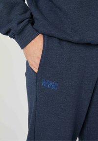 Meriharmaa collegekangasta, jossa on pehmeä tekstuuri, ja jonka vasemmalla puolella on sininen brodeerattu "American Vintage" -logo sekä sivutasku.