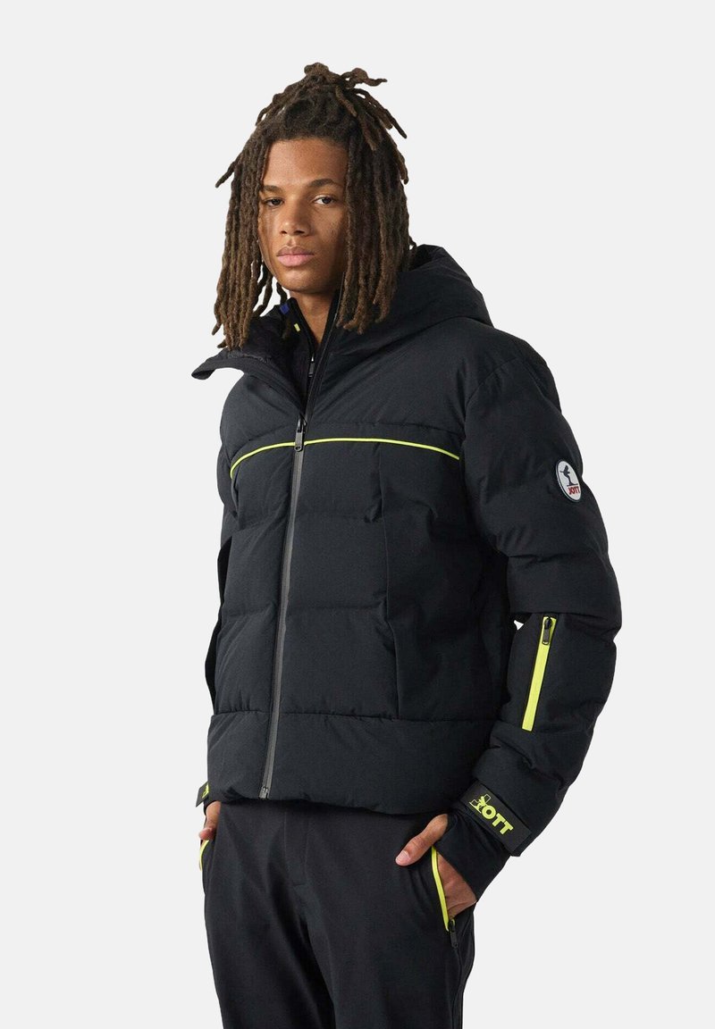 Zwarte pufferjas met limegroene accenten, rits aan de voorkant, geribbelde manchetten en logopatch op de mouw; voorzien van een capuchon en een doorgestikte textuur.
