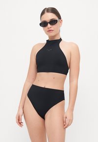 Fekete nyakpántos bikinifelső sima textúrával; magasan szabott fekete bikinialja. A modellen fekete napszemüveg van.
