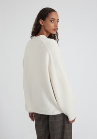 Pull oversize en maille crème avec ourlet et poignets côtelés. Présente un motif texturé et un col rond. Porté sur un pantalon à carreaux.