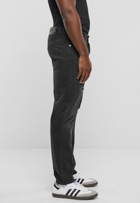 Musta farkkuhousut slim fit -mallilla, joissa on haalistunut pinta ja kulutuksia. Yhdistetty valkoisiin tennareihin ja mustaan paitaan.