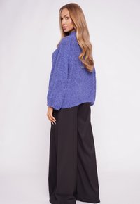 Blue textured jacket with long sleeves and a loose fit, paired with black wide-leg trousers. The design features a slightly cropped back.