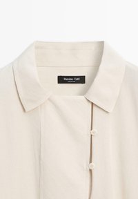 Beige overhemd met kraag en een zachte textuur, voorzien van een knoopsluiting en subtiele stikseldetails. Label zegt "Massimo Dutti."