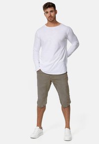Hvid langærmet bomulds skjorte kombineret med beige knæ-lange shorts og hvide sneakers. Enkel design med en afslappet pasform, uden synlige mønstre.