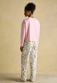 Mehka roza srajca z dolgimi rokavi v kombinaciji z kremnimi pižamami, ki imajo pisan motiv živali. Teksturna tkanina, sproščen kroj.