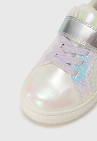 Spīdīga sporta apavu pāris ar varavīksnes krāsas virsmateriālu, lavandas krāsas šņorēm, sudraba krāsas siksniņu un zilu un baltu rakstu sānos. Apaļa purnas daļa un fakturēta zolīte.