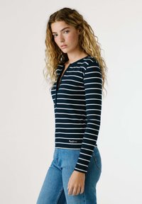 Námořnická a bílá pruhovaná dlouhá halenka s výstřihem Henley, která má knoflíkovou légou a žebrovanou strukturu, spárovaná se světle modrými džíny.