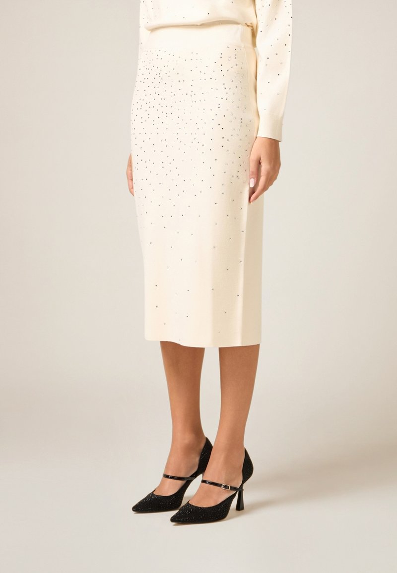 Gonna cremisi al ginocchio con strass argentati sparsi; abbinata a décolleté nere scintillanti con cinturino e punta affilata.