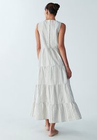 Gestreepte maxi-jurk van licht stof met gelaagde ruches, voorzien van een knoopsluiting aan de achterkant en een neutraal kleurenpalet met blauwe accenten.