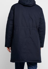 Granatowy, pikowany płaszcz z kapturem, z taliowaniem, długimi rękawami i gładką fakturą. Posiada prosty dół i delikatne detale przeszyć.