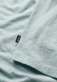 Jasnoniebieska bawełniana koszulka o miękkiej fakturze, z małą czarną metką naszytą po boku w pobliżu dołu.