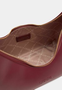 Borsa in pelle bordeaux con una cerniera dorata, caratterizzata da una superficie liscia e un rivestimento interno con logo stampato. L'interno offre ampio spazio per riporre gli oggetti.