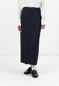 Jupe longue navy au cut straight, avec des plis sur le devant et des passants de ceinture. Associée à des mocassins noirs et des chaussettes blanches.
