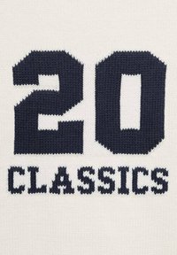 Knitted sweater featuring large navy blue text “20 CLASSICS” on a cream background, highlighting a contrasting color design and texture.