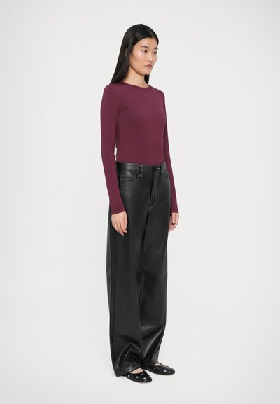 Langärmliges burgunderfarbenes Oberteil, kombiniert mit weit geschnittenen schwarzen Kunstlederhosen. Die Hose hat eine hohe Taille und sichtbare Nähte.