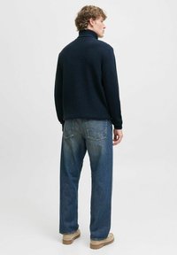 Pull en laine marine à col haut, associé à un jean bleu ample et des chaussures beige, vu de dos.