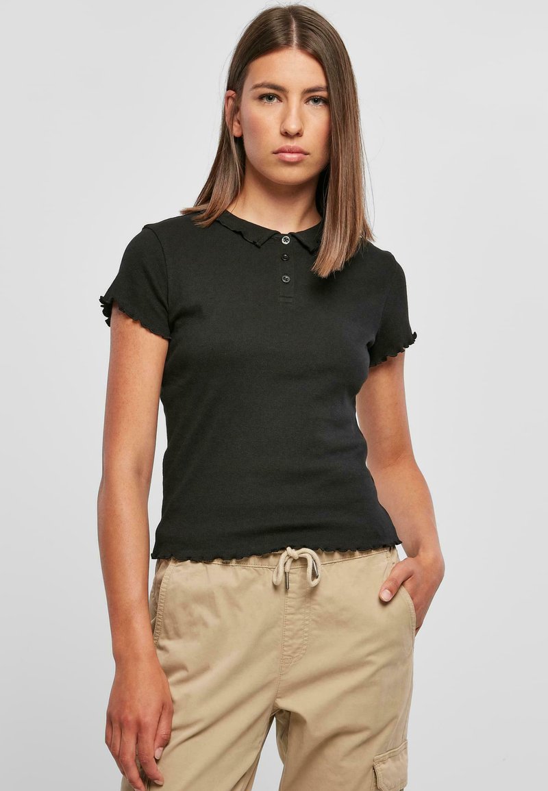 Svart polo skjorte med korte ermer, krage og bølgete kanter. Stoffet er ribbet og har tre knapper foran.