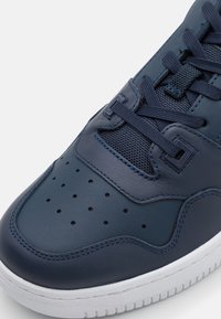 Sneaker in pelle blu navy con punta texturizzata, perforazioni per ventilazione, lacci piatti e suola in gomma bianca con motivo a scanalature.