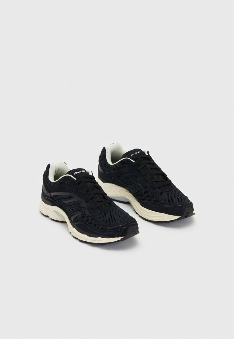 Zapatos deportivos negros con parte superior de malla y acentos de ante. Cuentan con una suela blanca acolchada y cordones negros. Diseño de punta redondeada.