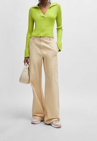 Zielona prążkowana bluzka z długim rękawem i kołnierzykiem, w zestawie z beżowymi spodniami cargo o szerokich nogawkach z bocznymi kieszeniami oraz neutralnymi sneakerami z różowymi akcentami.