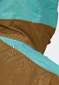 Gros plan sur un tissu imperméable bleu et marron avec des gouttelettes d'eau perlées à la surface, montrant la texture résistante à l'eau et le détail du matériau.