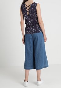 Navy ärmelloses Oberteil mit einem Herzdruck, tiefem Rücken und überkreuzten Trägern, kombiniert mit weiten Denim-Culottes und weißen Sneakers.