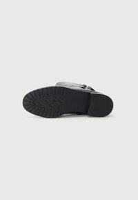 Black footwear with a textured rubber sole, smooth upper leather, and decorative strap detail. Rounded toe with low block heel.