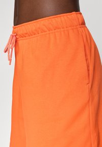 Oransje treningsshorts med elastisk midje og snor, sidelommer og et mykt, teksturert stoff.